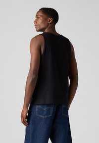 Débardeur noir sans manches en coton avec une coupe droite et une texture lisse. Présente un design minimaliste et une légère courbe à l'ourlet.