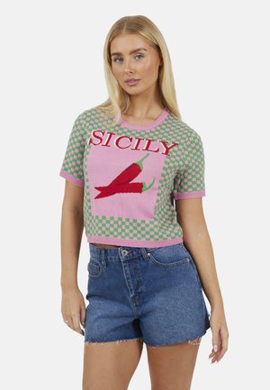 Giovane donna che indossa un maglione corto a quadri rosa e verde con peperoncini rossi e la scritta "SICILY", abbinato a pantaloncini di jeans blu.