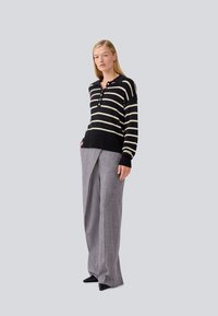Pull en maille rayé noir et ivoire avec un col et des boutons associé à un pantalon large plissé gris clair.