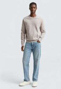 Ljust beige tröja med rund hals, bärs över ljusblå jeans. Avslappnade vita sneakers kompletterar outfiten. Enkla, släta texturer överallt.