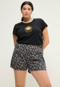 T-shirt noir en coton avec un graphique de soleil doré portant l'inscription "RESPIRER FACILEMENT", associé à un short bleu marine orné d'un motif de soleil en crème.