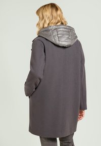 Abrigo gris con capucha acolchada, tejido texturizado y forma estructurada. El abrigo cuenta con cierre de botones ocultos y bolsillos laterales.