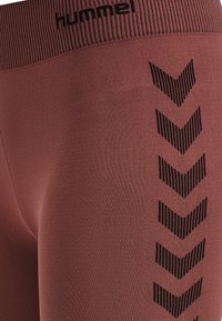 Bordeaux leggings met een geribde tailleband hebben zwarte zigzagpatronen langs de zijkant, gemaakt van een gladde, rekbare stof.