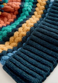 Mehrfarbiger Strickstoff mit einem geflochtenen Muster in Grün-, Orange- und Goldtönen, sowie einer dunkelblauen gerippten Textur am Rand.