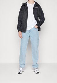 Czarna lekka kurtka zapinana na zamek z kapturem, noszona na białej koszulce i jasnoniebieskich, luźnych dżinsach, w połączeniu z białymi trampkami.