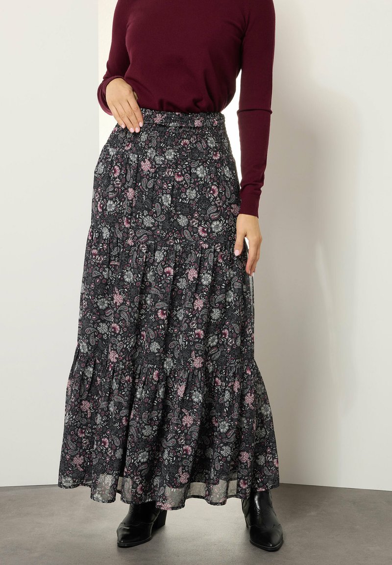 Maxi rok van zwarte stof met een bloemenpatroon in roze en wit. Het heeft een geraffineerde taille en een gelaagde zoom. Gecombineerd met zwarte laarzen.