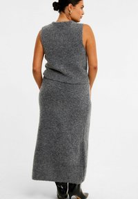 Gray knit sleeveless top paired with a matching long skirt, featuring a soft texture and a fitted silhouette. Black ankle boots visible.
