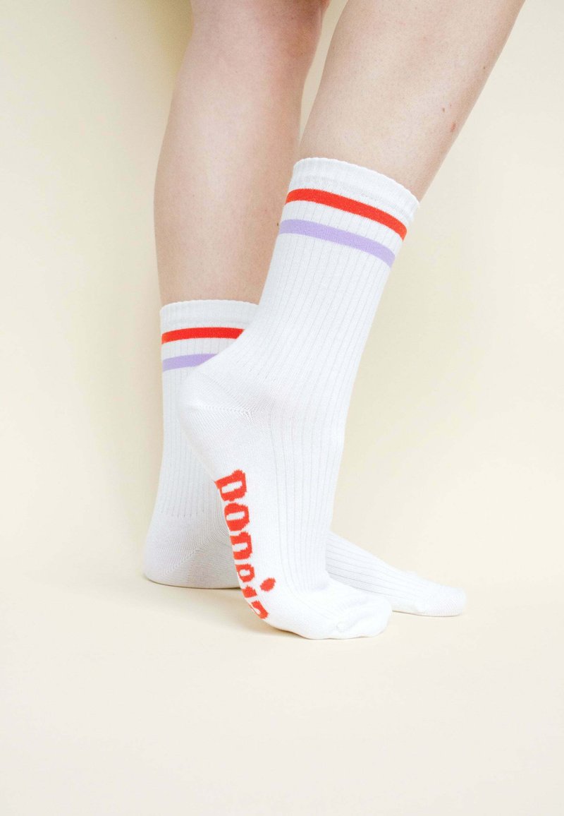 Weiße gerippte Socken mit roten, orangefarbenen und lila Streifen am Bund, mit dem Wort "Dona" in fettem Rot an der Ferse.