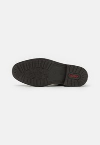 Suela de zapato de goma negra con patrones de agarre texturizados y un logo en relieve en rojo. Presenta un perfil plano y elementos de tracción distintivos.