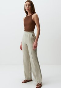 Top a canotta marrone a coste abbinato a pantaloni larghi beige chiaro. I pantaloni hanno una vestibilità rilassata e una vita elastica. Sandali marroni completano l'outfit.