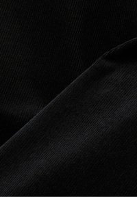 Gros plan sur un tissu noir côtelé avec un pli diagonal, montrant la texture et les détails du matériau doux.