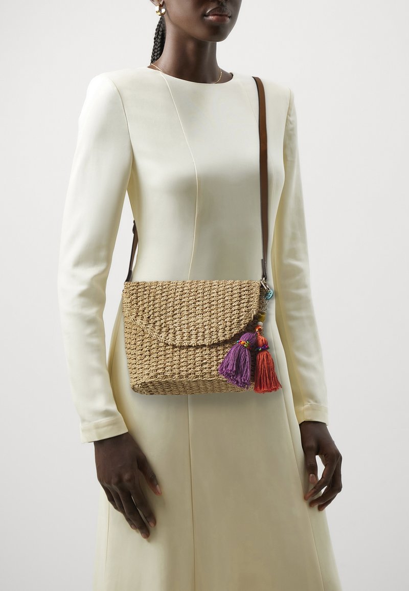Borsa a tracolla intrecciata in paglia con chiusura a patta, decorata con nappine colorate viola e rosse. Tracolla marrone e superficie con dettagli testurizzati.