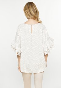 Blusa leggera e strutturata in un morbido bianco sporco con un sottile motivo a foglia. Presenta maniche arricciate e un'apertura a chiave con bottoni sulla schiena.