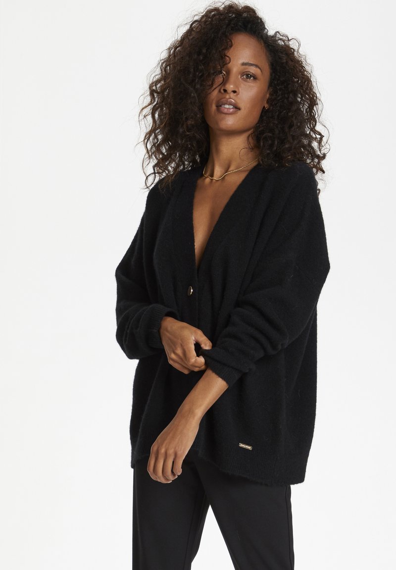 Black oversized cardigan with a deep V-neck, featuring a single button closure and ribbed cuffs. Soft texture and minimalist design.