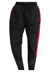 Zwarte sportbroek met rode zijstrepen, elastische tailleband en trekkoord. Heeft getextureerde zwarte onderste panelen met een gespikkeld patroon.