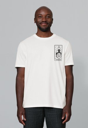 Witte katoenen t-shirt met een grafisch ontwerp van een vrouw en een leeuw, met het label "VIII STRENGTH" op de linkerborst. Korte mouwen, ronde hals.