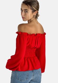 Blusa rossa scollata sulle spalle con bordi arricciati e vita elasticizzata, caratterizzata da maniche lunghe e una vestibilità comoda. Tessuto leggero.