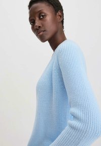 Vaaleansininen neulepaita, jossa on leveä pääntie ja pitkät hihat, joissa on tekstuurikuvio ja ribbireunat.