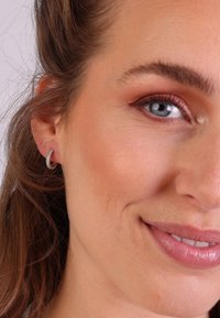 Zilveren oorbellen met een gedraaide design, die fijne details en een glanzende gepolijste afwerking tonen. De huidtint lijkt licht met natuurlijke make-up.