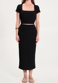 Czarny dwuczęściowy strój składający się z dopasowanego topu z kwadratowym dekoltem oraz spódnicy o wysokim stanie do kolan, wykonanej z fakturowanej tkaniny.