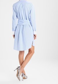 Blau-weiß gestreiftes Hemdkleid mit langen Ärmeln, tailliertem Gürtel und seitlichen Schlitzen; kombiniert mit silbernen High Heels.