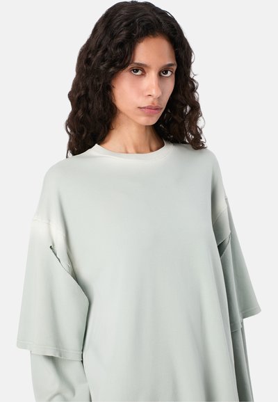 Oversized lichtgroen T-shirt van zachte stof met wijde mouwen en een ronde hals. Heeft een losse pasvorm en subtiele gestikte accenten.