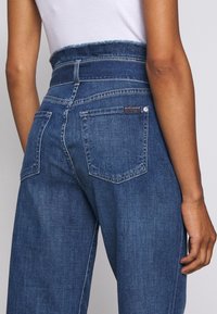 Jeansy z wysokim stanem w niebieskim denimie o luźnym kroju, z tylnymi kieszeniami, przeszyciami oraz metką przy pasku.