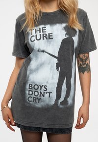 Black graphic t-shirt featuring a faded design with a silhouette holding a guitar and text "THE CURE BOYS DON'T CRY" in bold letters.
