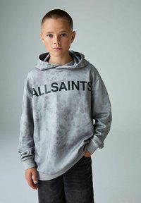 Šedá mikina s zavazovacím kapucím a klokaní kapsou, s černým logem "ALLSAINTS" na hrudi. Kombinováno s tmavými džíny.