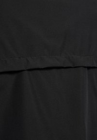 Schwarzer Stoff mit glatter Textur. Verfügt über eine horizontale Naht für das Design. Insgesamt ein schlichtes und minimalistisches Erscheinungsbild ohne Muster.