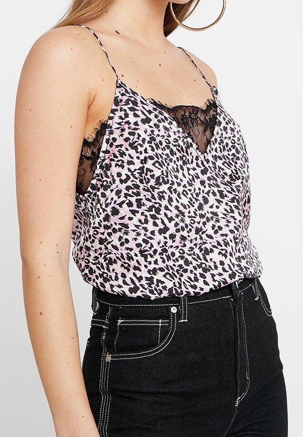 Top med pink leopardmønster, blondekant ved halsen, tynde justerbare stropper og letvægtsstof. Båret over højtaljede sorte jeans.