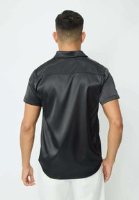 Chemise noire à manches courtes en tissu lisse, dotée d'un col et d'un ourlet arrondi. Le dos présente un design sans couture sans accents supplémentaires.