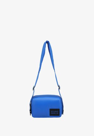 Mėlyna sintetinio audinio kryžminė rankinė, uždarymo užtrauktukas, reguliuojama juosta ir juodas logotipo pleistras priekyje.