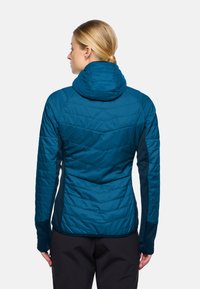Teal geïsoleerde jas met een capuchon, voorzien van een chevron-quiltpatroon en contrasterende donkere mouwen. Gladde textuur met een getailleerd ontwerp.