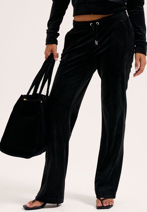 Zwarte velours broek met een relaxte pasvorm, voorzien van een elastische tailleband,koord en zijzakken, gecombineerd met een zwarte tote tas.