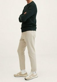 Ciemnozielony sweter z dzianiny, beżowe spodnie zwężane oraz beżowe trampki z białymi akcentami. Luźny krój, teksturowana tkanina i prosty design.