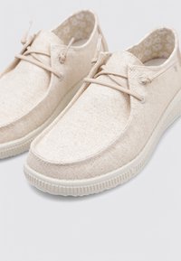 Zapatillas de lona beige con un acabado texturizado, puntera redonda y diseño con cordones. Suela de goma con bordes estriados y forro interior con un patrón floral.