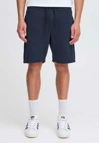 Shorts en coton bleu marine avec une taille élastique et un cordon de serrage, dotés de poches latérales et d'une coupe décontractée, se terminant juste au-dessus des genoux.