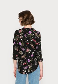 Blusa preta com flores coloridas, mangas três quartos, tecido macio, corte relaxado e bainha redonda.