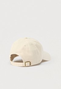 Μπεζ βαμβακερό καπέλο με κυρτή γείσο, ρυθμιζόμενο λουράκι στο πίσω μέρος και λεπτομέρειες ραφής. Ομαλή υφή και κλασικό σχέδιο.