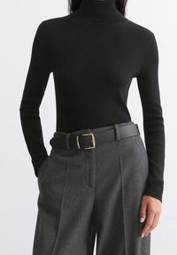 Pull à col roulé noir côtelé associé à un pantalon gris taille haute et une ceinture noire avec une boucle dorée. Texture de tissu lisse.