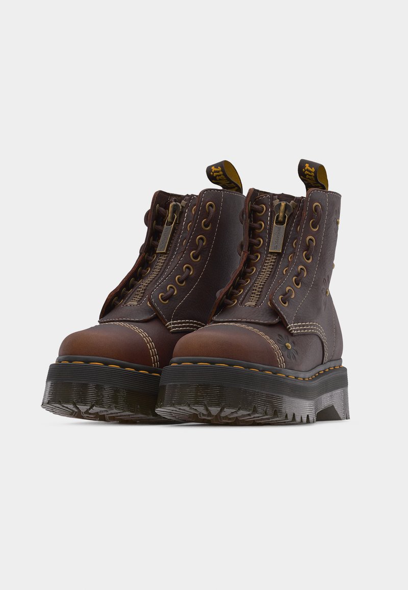 Brown leather ankle boots with thick black soles, front zippers, lace-up sides, contrast stitching, and yellow pull tabs at the back.