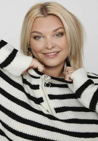 Schwarz-weiß gestreifter Reißverschluss-Pullover mit hohem Kragen und gerippten Bündchen. Weiche Stricktextur mit einem Reißverschluss-Detail vorne.