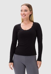 Czarny top z długim rękawem o teksturze prążkowanej, z koronkowym dekoltem w kształcie falbanek i dopasowanym kroju. W zestawie z szarymi legginsami.