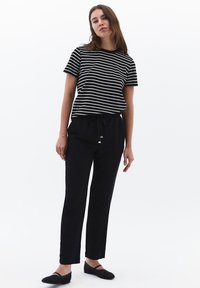 Schwarz-weiß gestreiftes T-Shirt kombiniert mit schwarzen Jogginghosen. Das Modell trägt schwarze geflochtene Ballerinas. Glatter Stoff, lockerer Schnitt, lässiger Stil.