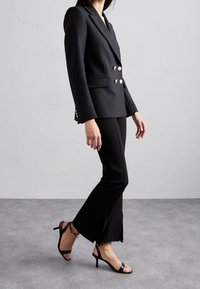 Blazer nero doppiopetto con bottoni dorati, vestibilità tailored e pantaloni neri a campana. Completato con sandali neri con tacco alto.