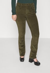 Olivově zelené kordové kalhoty se slim fit střihem, s pěti kapsami a zapínáním na knoflík. Společně s černými botami na blokovém podpatku.