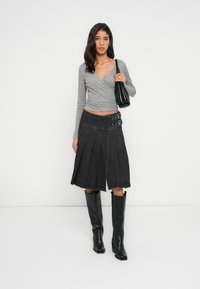 Γκρι τοπ τύπου wrap, σκουρόχρωμη φούστα από τζιν με πιέτες και λεπτομέρεια με αγκράφα, και μαύρες ψηλές μπότες με τακούνι μέχρι τον μηρό, συνοδευόμενα από μια μικρή μαύρη τσάντα χειρός.