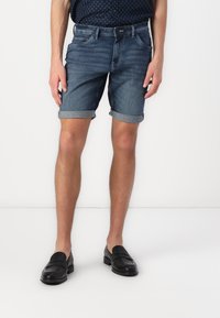 Shorts en denim dans un lavage bleu foncé, avec des ourlets retournés et cinq poches, associés à des mocassins en cuir noirs. Texture lisse et coupe décontractée.
