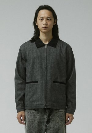 Gray zip-up jacket with a black collar, two front pockets, and a slightly textured finish. Worn over matching light gray pants.